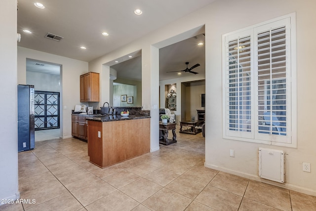 kitchen featuring sink, ceiling fan, dark stone countertops, light tile patterned floors, and fridge