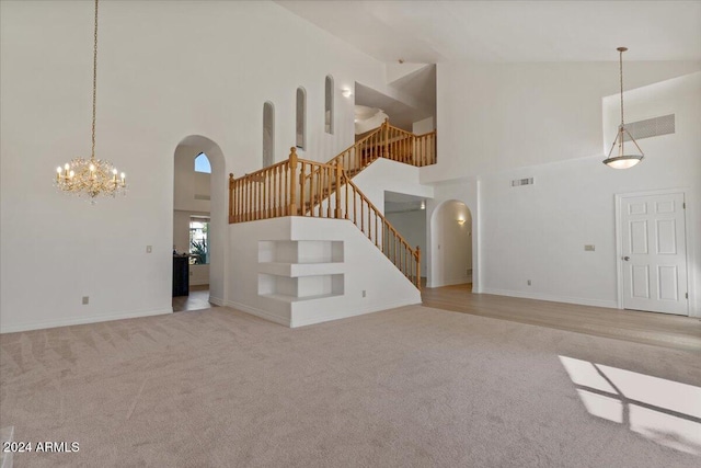 unfurnished living room with a notable chandelier, a towering ceiling, and light carpet