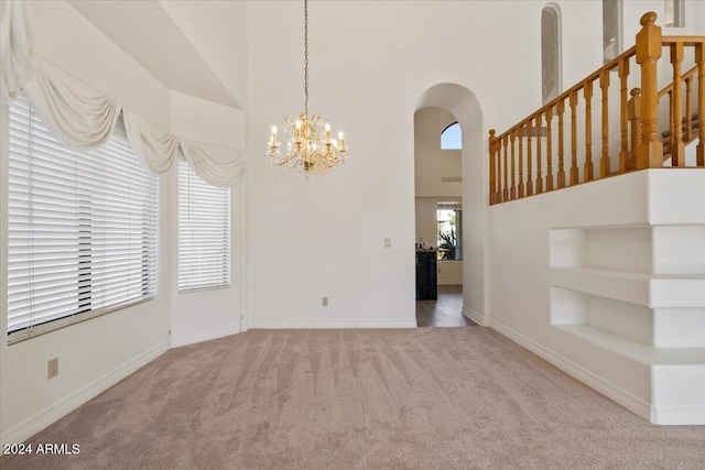 carpeted empty room featuring built in features, a towering ceiling, and an inviting chandelier