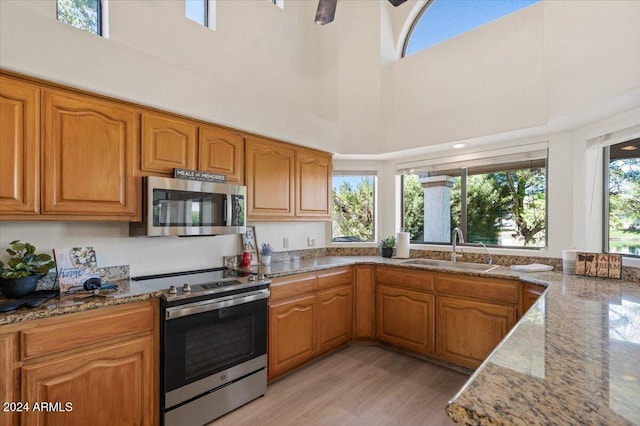 kitchen featuring a towering ceiling, stainless steel appliances, light stone counters, and sink