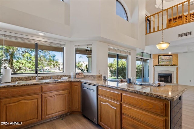 kitchen with sink, light hardwood / wood-style flooring, stainless steel dishwasher, a towering ceiling, and stone countertops