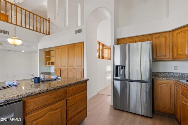 kitchen with light stone countertops, a high ceiling, stainless steel refrigerator with ice dispenser, light hardwood / wood-style floors, and decorative light fixtures