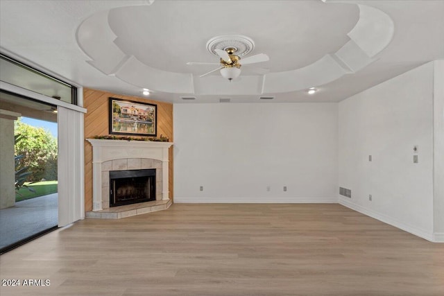 unfurnished living room with a raised ceiling, ceiling fan, a fireplace, and light hardwood / wood-style floors