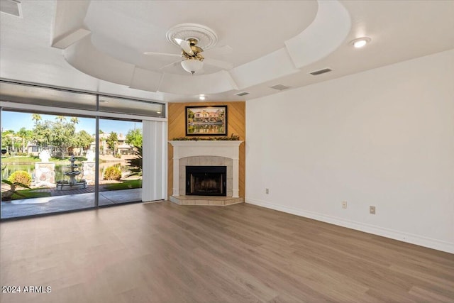 unfurnished living room with ceiling fan, a raised ceiling, wood-type flooring, and a tile fireplace