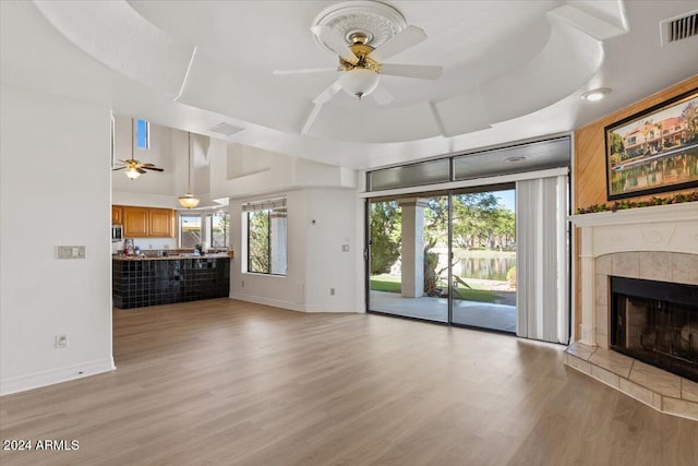 unfurnished living room featuring a wealth of natural light, ceiling fan, a raised ceiling, and a tile fireplace