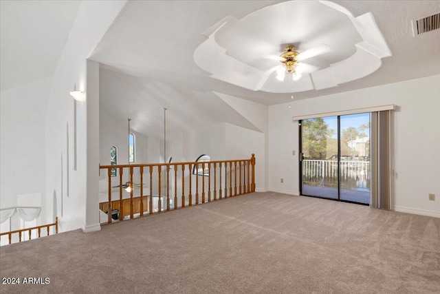 unfurnished room featuring ceiling fan, light colored carpet, lofted ceiling, and a tray ceiling