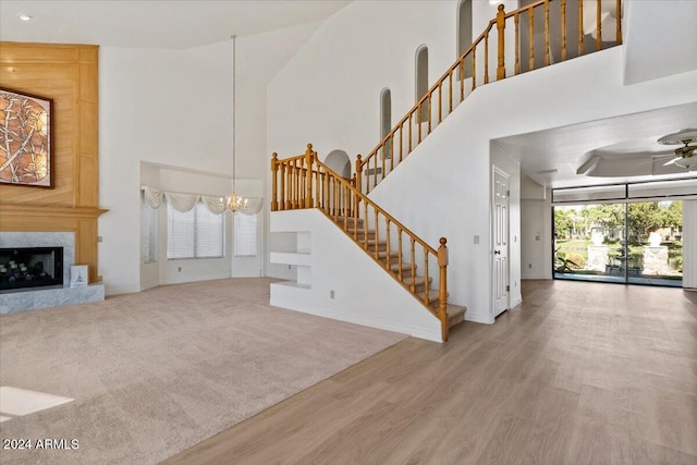 unfurnished living room with a fireplace, a high ceiling, ceiling fan with notable chandelier, and hardwood / wood-style floors