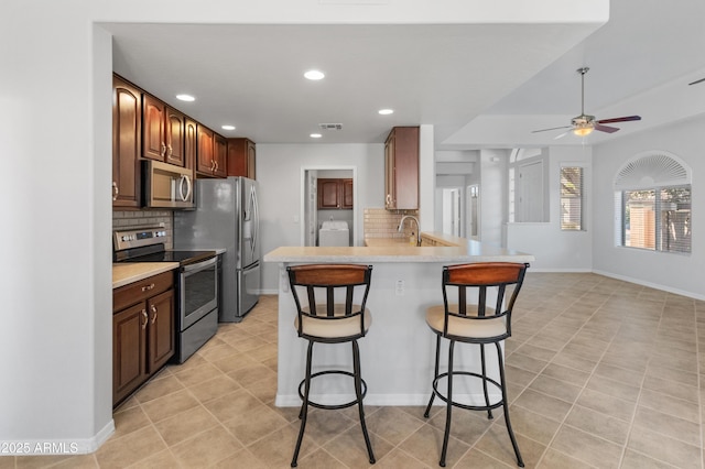 kitchen featuring a breakfast bar, appliances with stainless steel finishes, light tile patterned flooring, decorative backsplash, and kitchen peninsula