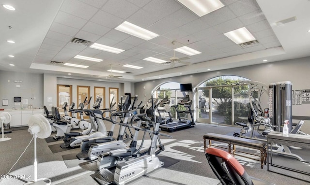 workout area with ceiling fan, a raised ceiling, and a drop ceiling