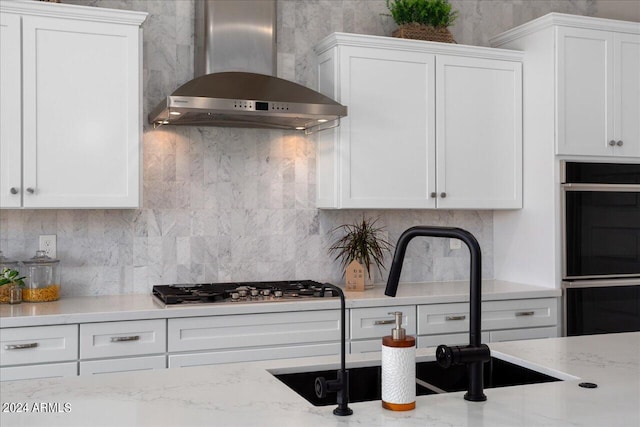 kitchen with backsplash, appliances with stainless steel finishes, wall chimney exhaust hood, and white cabinetry