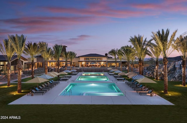 pool at dusk with a yard, a patio area, and a hot tub