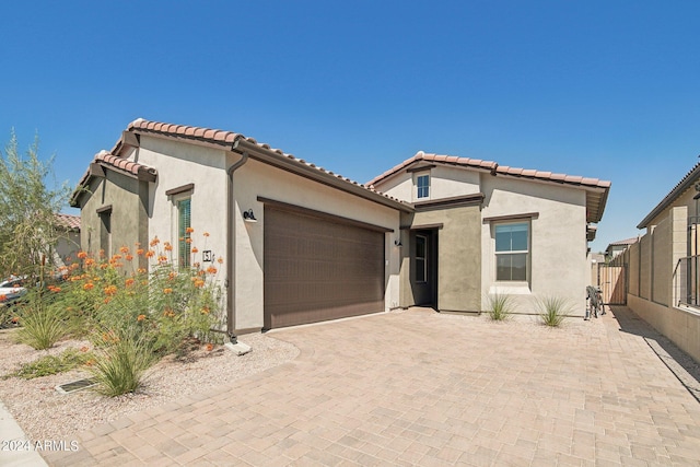 mediterranean / spanish home with a tiled roof, decorative driveway, an attached garage, and stucco siding