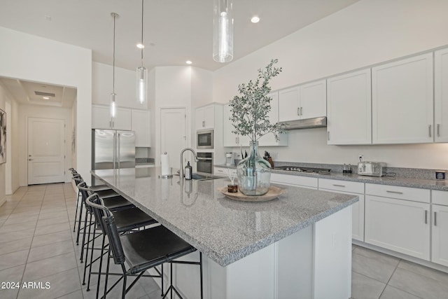 kitchen featuring under cabinet range hood, light tile patterned floors, white cabinets, and built in appliances