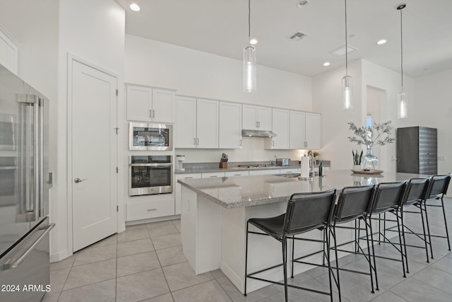 kitchen with stainless steel appliances, visible vents, a towering ceiling, a sink, and under cabinet range hood