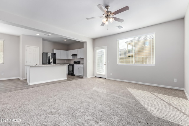 unfurnished living room with light colored carpet and ceiling fan