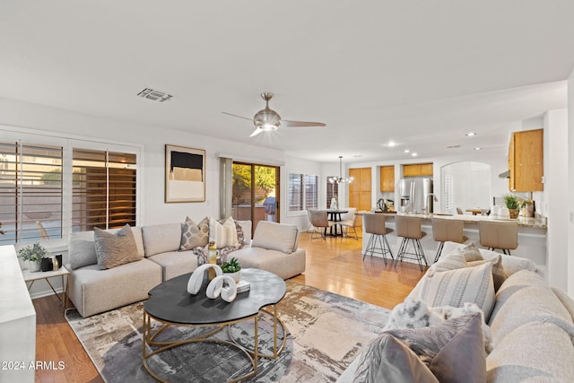 living room with ceiling fan with notable chandelier, sink, and light hardwood / wood-style flooring