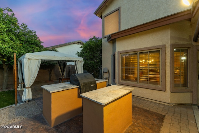 patio terrace at dusk featuring a gazebo, grilling area, and exterior kitchen