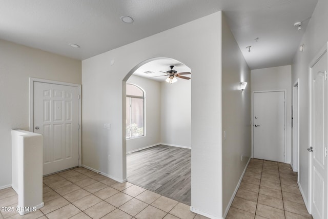 hallway with arched walkways, baseboards, visible vents, and light tile patterned flooring