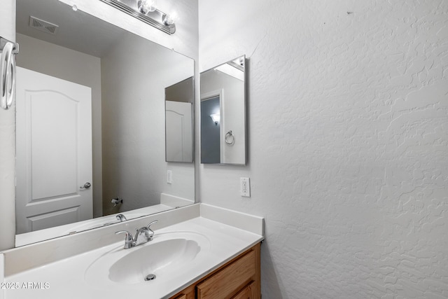 bathroom with vanity, a textured wall, and visible vents