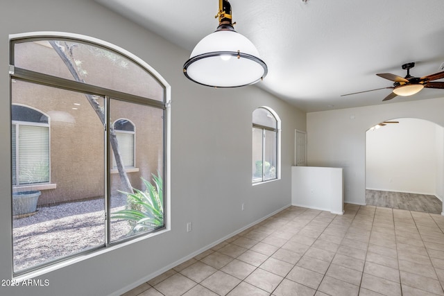 unfurnished room with arched walkways, a ceiling fan, baseboards, and tile patterned flooring