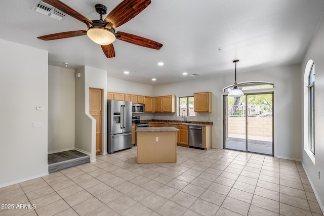 kitchen with appliances with stainless steel finishes, a sink, a center island, baseboards, and visible vents