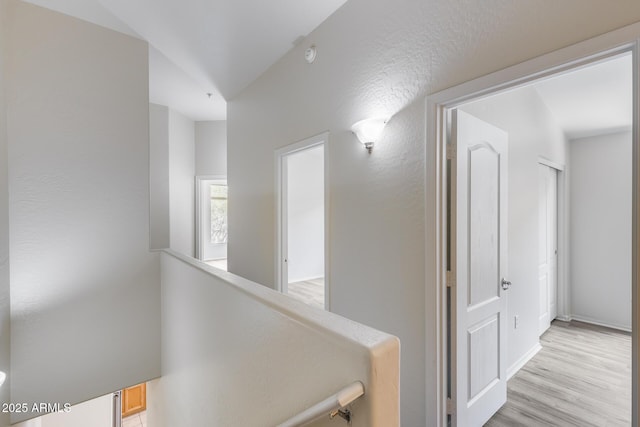 corridor with light wood-type flooring, baseboards, and an upstairs landing
