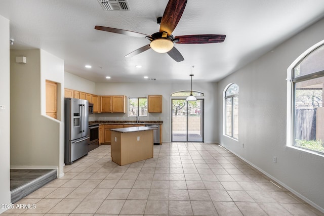 kitchen with ceiling fan, a kitchen island, visible vents, baseboards, and stainless steel appliances