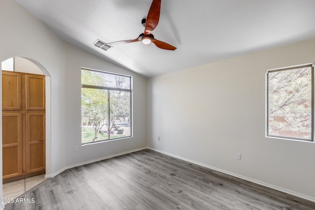 unfurnished room with visible vents, ceiling fan, light wood-type flooring, arched walkways, and vaulted ceiling