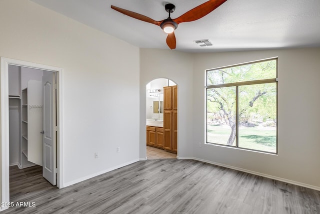 unfurnished bedroom featuring a walk in closet, visible vents, arched walkways, baseboards, and light wood-style floors