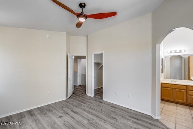 unfurnished bedroom with light wood-style floors, arched walkways, baseboards, and ensuite bath