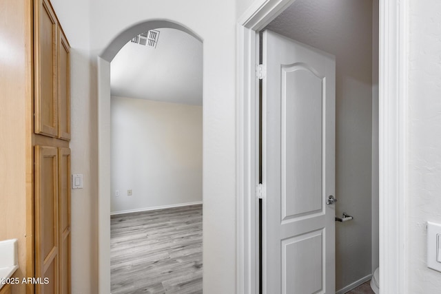 corridor with arched walkways, baseboards, visible vents, and wood finished floors