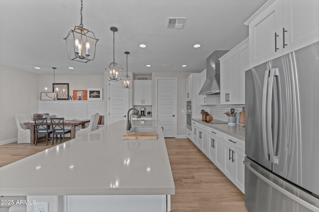 kitchen featuring wall chimney exhaust hood, sink, hanging light fixtures, a large island with sink, and stainless steel appliances