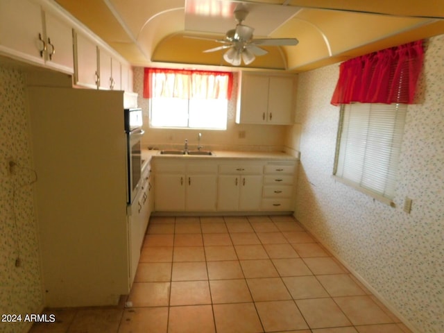 kitchen with light tile patterned floors, oven, white cabinetry, and sink