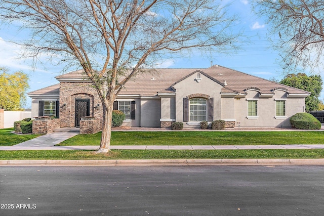 mediterranean / spanish home featuring stone siding, a front yard, fence, and stucco siding