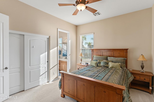 bedroom with ceiling fan, ensuite bath, visible vents, and light colored carpet