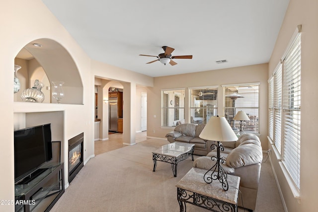 living room featuring baseboards, visible vents, a ceiling fan, a glass covered fireplace, and carpet floors