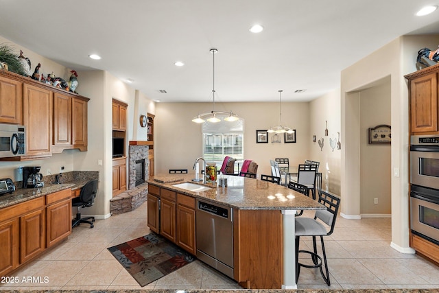 kitchen featuring stainless steel appliances, a breakfast bar, a sink, brown cabinets, and a center island with sink