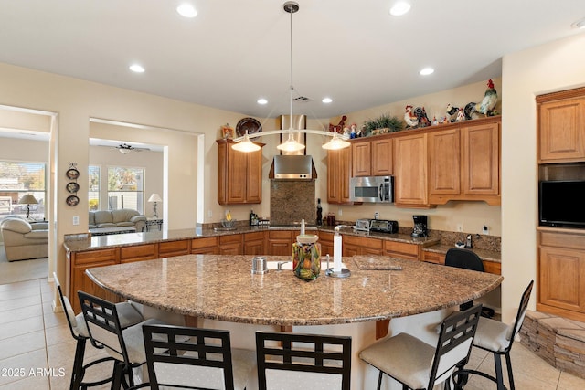 kitchen featuring brown cabinetry, stainless steel microwave, a kitchen breakfast bar, and recessed lighting