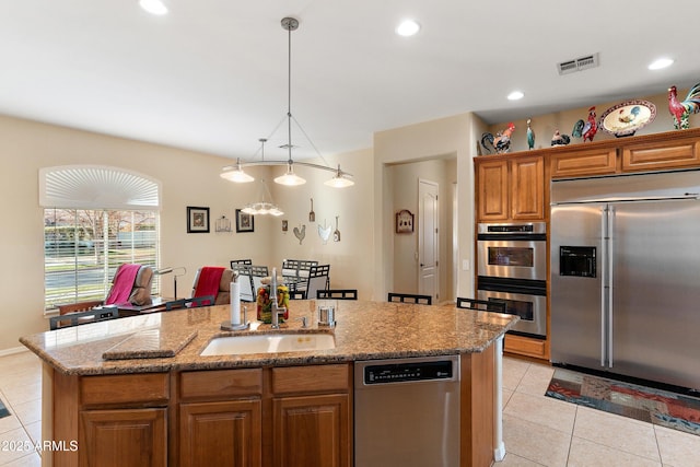 kitchen with a center island with sink, light tile patterned floors, visible vents, appliances with stainless steel finishes, and a sink