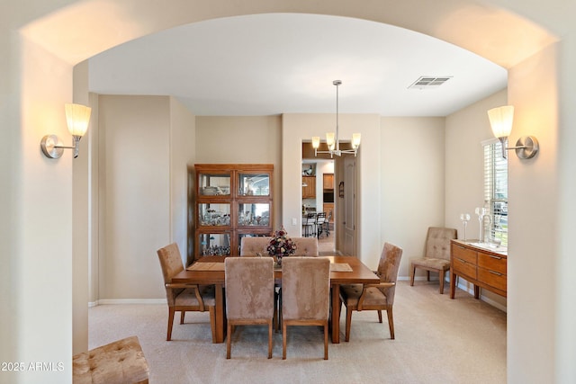 dining area featuring arched walkways, light colored carpet, a notable chandelier, visible vents, and baseboards