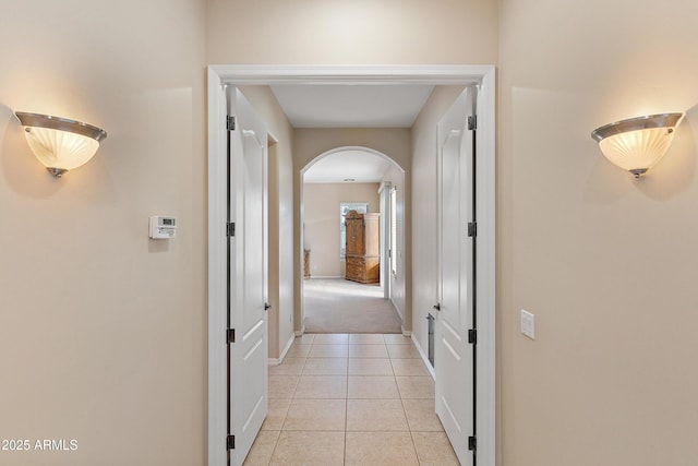 hall featuring baseboards, arched walkways, and light tile patterned flooring