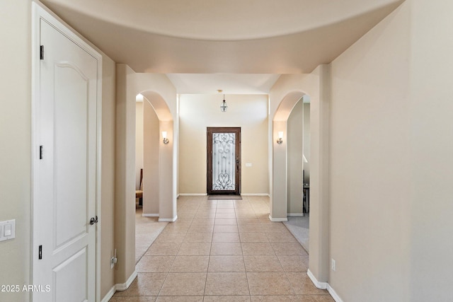 entryway featuring arched walkways, light tile patterned flooring, and baseboards