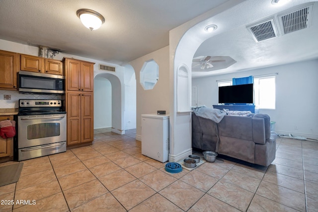 kitchen with ceiling fan, backsplash, a textured ceiling, light tile patterned floors, and appliances with stainless steel finishes