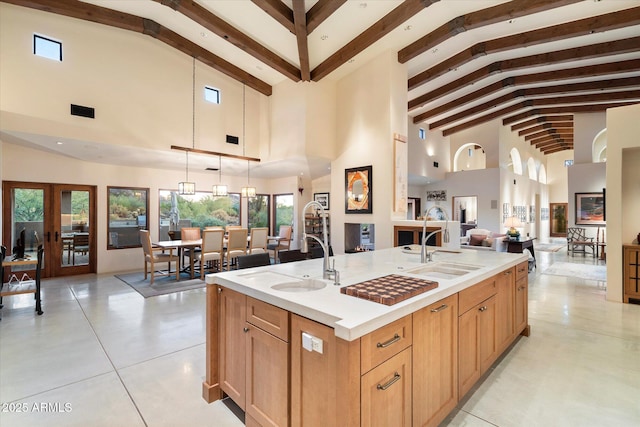 kitchen featuring french doors, sink, hanging light fixtures, beamed ceiling, and a kitchen island with sink