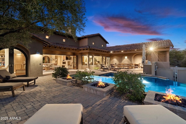 pool at dusk featuring a fire pit and a patio