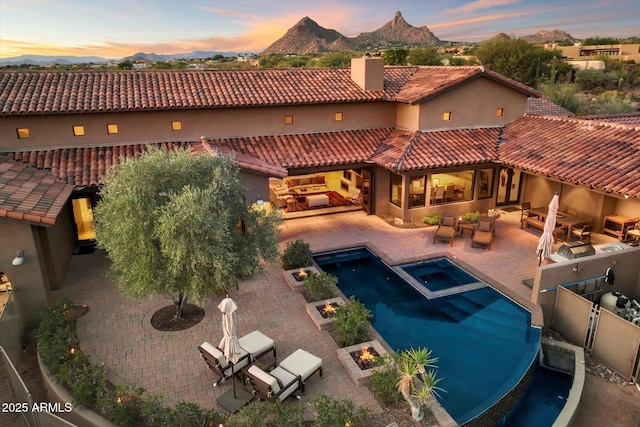 pool at dusk featuring an in ground hot tub, outdoor lounge area, a mountain view, and a patio