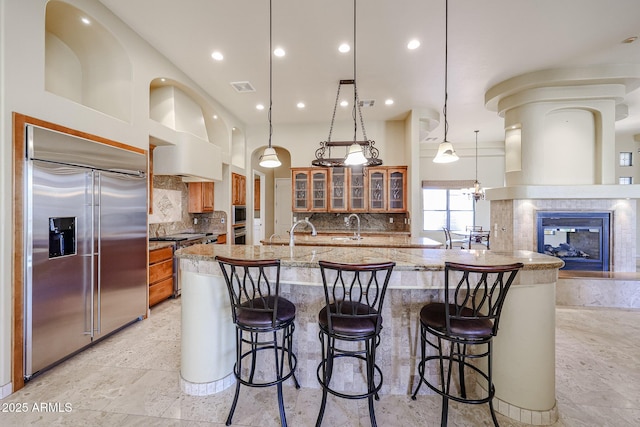 kitchen featuring pendant lighting, a kitchen bar, built in appliances, and light stone countertops