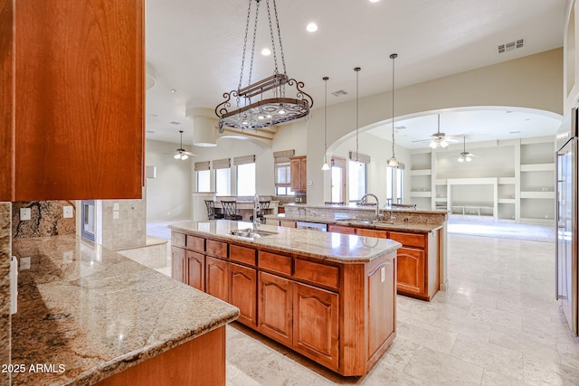 kitchen featuring sink, ceiling fan, hanging light fixtures, light stone countertops, and an island with sink