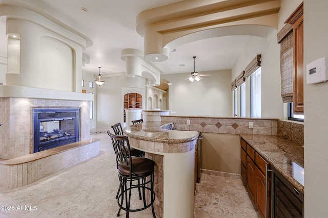 kitchen featuring pendant lighting, a fireplace, a breakfast bar area, and ceiling fan