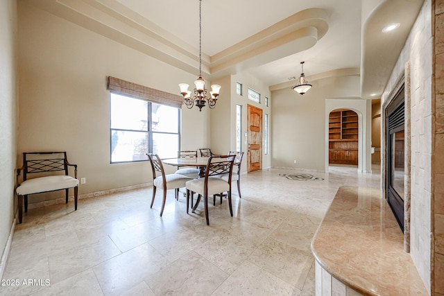 dining room featuring an inviting chandelier, built in features, a raised ceiling, and a high ceiling